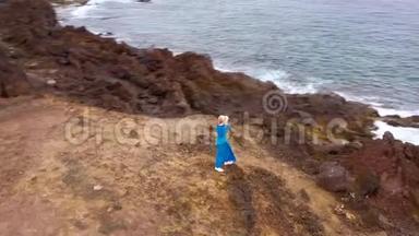在海岸的一个保护区，一位身穿漂亮蓝裙和帽子的女士<strong>站在山顶</strong>上观看空中风景